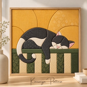 Peut inclure: Une œuvre d'art textile carrée encadrée présentant un motif Kinusaiga d'un chat noir et blanc endormi. Le chat repose sur une surface rayée verte et crème sur un fond jaune avec un imprimé floral subtil, le tout dans un cadre en bois clair.