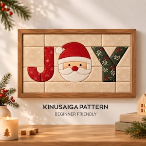 May include: A rectangular wooden framed wall art piece featuring a Kinusaiga pattern that spells the word JOY. The letter J is red with white snowflakes, the O is a Santa Claus face, and the Y is dark green with red berries and leaves.