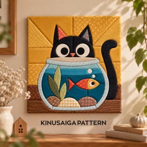 Op de afbeelding: Een vierkant wandkleed van stof met een Kinusaiga-patroon van een zwarte kat die in een blauwe vissenkom kijkt. De kat heeft grote witte ogen en een roze neus. In de kom zwemt een oranje vis tussen groene bladeren en kiezels door.