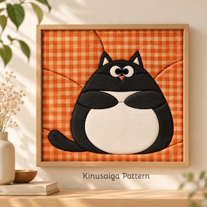 May include: A square framed wall art piece featuring a Kinusaiga pattern of a round black and white cat against an orange and white gingham background. The cat has large white eyes with black pupils and a small pink nose, set in a light wood frame.