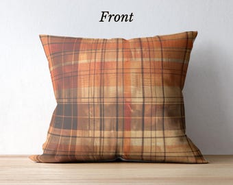 May include: Square decorative pillow with a plaid pattern in shades of orange, brown, and tan. The word "Front" is printed in black on the white background. The pillow is placed on a wooden surface.