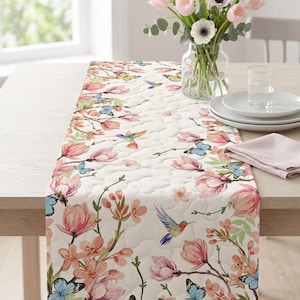 Peut inclure: Chemin de table floral avec un motif matelassé, orné de fleurs roses, de papillons bleus et de colibris. Le chemin de table est posé sur une table en bois clair, avec un vase de tulipes roses et d'anémones blanches en arrière-plan.