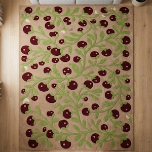 May include: A rectangular area rug with a beige background and a repeating pattern of green vines and burgundy berry-like shapes. The rug is placed on a wooden floor, with a gray sofa visible in the background.