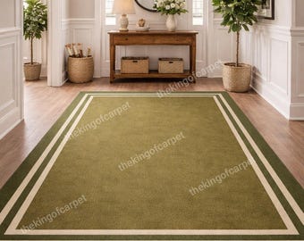 May include: A rectangular area rug featuring a solid olive green center bordered by a thin white line and a wider olive green outer frame. The rug is positioned on a wooden floor and displays the repeating watermark text thekingofcarpet.