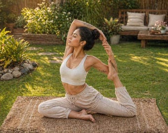 May include: A woman doing yoga on a brown rectangular mat in a sunny outdoor setting. She is wearing a white sports bra and light-colored pants. The background includes green grass, trees, and a wooden bench.