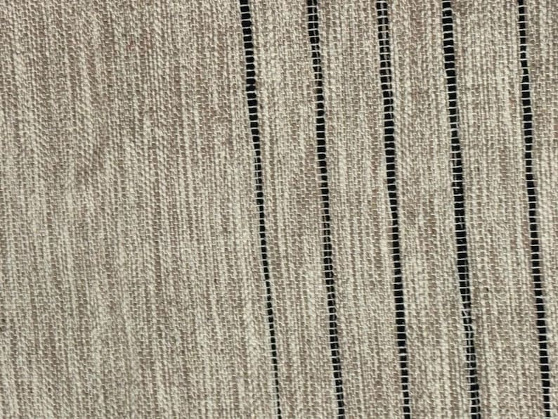 May include: A textured fabric featuring a light beige, woven surface with a series of vertical, thin black stripes. The material displays a visible cross-hatch pattern throughout the beige sections, contrasted by the open, ladder-like weave of the black lines.