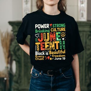 Może przedstawiać: Czarny t-shirt z kolorowym wzorem graficznym. Projekt zawiera słowa "POWER", "JUNE TEENTH" i "Black is Beautiful". Koszulka zawiera r&oacute;wnież serca, gwiazdy i inne symbole. Tekst "June 19" jest r&oacute;wnież uwzględniony.
