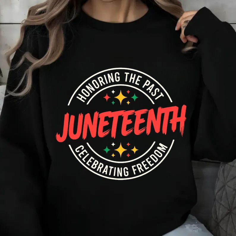 Może przedstawiać: Czarna bluza z okrągłą grafiką z napisem "Honoring the Past, Juneteenth, Celebrating Freedom". Tekst jest czerwony i biały, z kolorowymi akcentami gwiazd. Projekt upamiętniający Juneteenth.