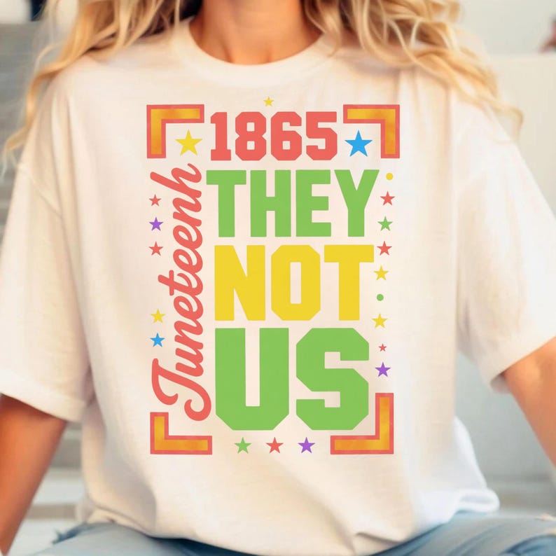 Może przedstawiać: Biała koszulka z napisem "1865 THEY NOT US" w kolorze czerwonym, zielonym, ż&oacute;łtym i zielonym. Słowo "Juneteenth" jest wydrukowane pionowo na czerwono po lewej stronie. Kolorowe gwiazdy otaczają tekst.