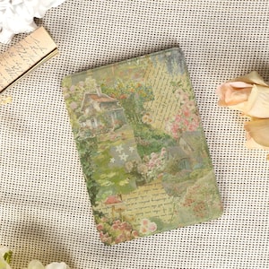 Peut inclure: Un journal rectangulaire avec un motif de cottage et de jardin vintage. La couverture présente une illustration à l'aquarelle d'une maison entourée de fleurs et de verdure, avec un texte manuscrit superposé. La palette de couleurs comprend des verts, des roses et des crèmes.