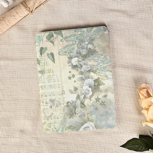 Peut inclure: Un objet décoratif rectangulaire avec un motif floral et de notes de musique. Le motif présente des roses bleu clair, des feuilles vertes et des notes de musique sur un fond crème. L'objet est entouré d'un tissu beige.