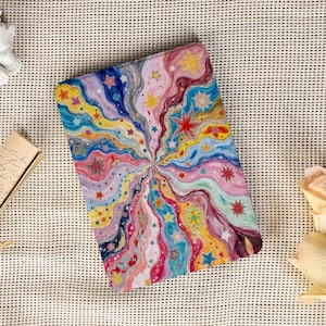 May include: A colorful, abstract art piece featuring a vibrant explosion of stars and swirling patterns in shades of blue, pink, yellow, and red. The artwork is on a rectangular surface, possibly a notebook or tablet cover.