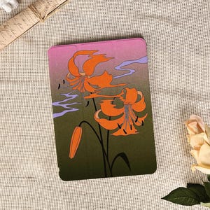 May include: A tablet case featuring a floral design with orange lilies against a gradient background of pink, purple, and green. The case has a black stem and leaves, with a hint of blue. The overall aesthetic is reminiscent of Japanese art.