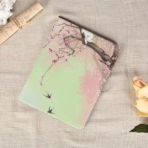 Puede incluir: Una funda para tableta con un diseño de acuarela de un cerezo en flor con flores rosas y dos golondrinas en vuelo sobre un fondo verde y rosa. La funda tiene un acabado liso y un diseño protector.