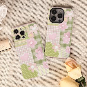 May include: Two phone cases with a patchwork design featuring pink flowers, hearts, and green gingham and polka dot patterns. The cases have a soft, pastel color palette and a whimsical, feminine aesthetic.