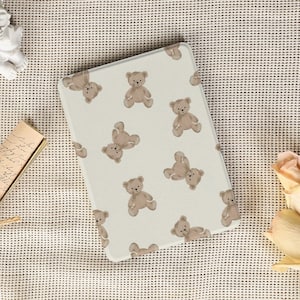 May include: An off-white tablet case with a repeating pattern of light brown teddy bears. The bears are in different poses against a neutral background. The case is designed to protect a tablet or e-reader. The case is approximately 20 cm x 13 cm.