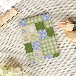 May include: A patchwork design notebook with squares of green gingham, blue floral, and green diamond patterns. The notebook includes a square with a white bunny, a yellow tulip, and a four-leaf clover.