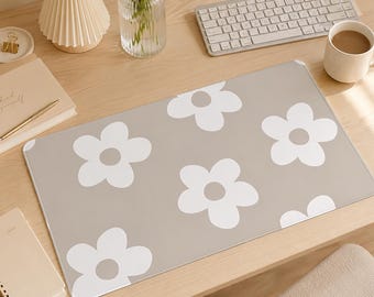 May include: A rectangular desk mat featuring a repeating pattern of large, white, five-petaled flowers with light gray centers set against a solid, muted beige background. The mat has rounded corners and a smooth, flat surface texture.