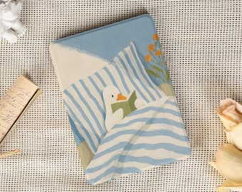 May include: A rectangular e-reader case featuring a light blue and white striped pattern with a white duck illustration reading a green book while tucked into bed, accented by small orange flowers on a light blue background.