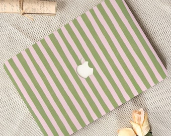 May include: A laptop with a green and pink striped design. The Apple logo is visible in the center. The laptop is on a textured surface with a scroll and flowers.