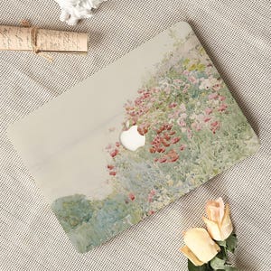 May include: A laptop skin featuring an impressionist-style painting of a garden with soft green foliage and clusters of pink and red flowers. The design includes a circular cutout in the centre for the Apple logo, set against a light background.