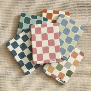 Può includere: Una collezione di sottobicchieri rettangolari con un motivo a scacchi in vari colori, tra cui rosa, blu, verde e arancione. Alcuni sottobicchieri hanno nomi scritti a mano e il testo "Jace Gift".