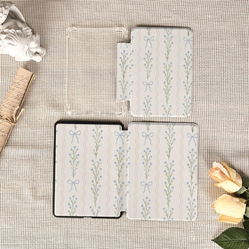 May include: A set of phone cases and a clear phone cover. The cases feature a white background with a repeating pattern of light blue bows and floral stems. The clear cover is visible in the image.