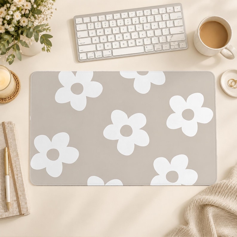 Puede incluir: Una alfombrilla de escritorio rectangular con un fondo beige claro y un patr&oacute;n repetitivo de grandes flores blancas de cinco p&eacute;talos. La alfombrilla tiene una superficie lisa y plana con esquinas redondeadas, ofreciendo un dise&ntilde;o sencillo.