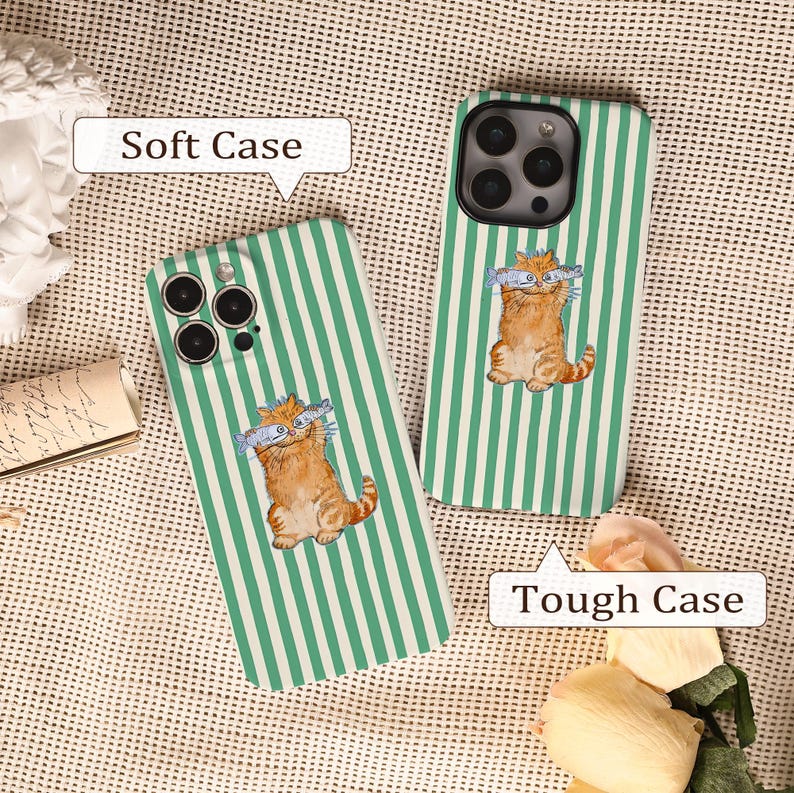 May include: Two phone cases with a green and white striped design. One case is labelled "Soft Case" and the other "Tough Case". Each case features an orange cartoon cat holding two fish. The cases are on a textured surface.