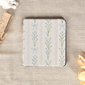 May include: A floral-patterned tablet case featuring a design of light blue flowers and bows on a cream background. The case has a black border and a vertical striped pattern. The overall aesthetic is delicate and feminine.