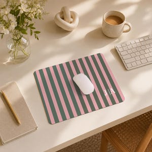 May include: A rectangular mouse pad featuring a pattern of vertical stripes in alternating shades of dusty pink and dark sage green. The bottom right corner of the mouse pad displays the white capital letters J and A separated by a vertical line.