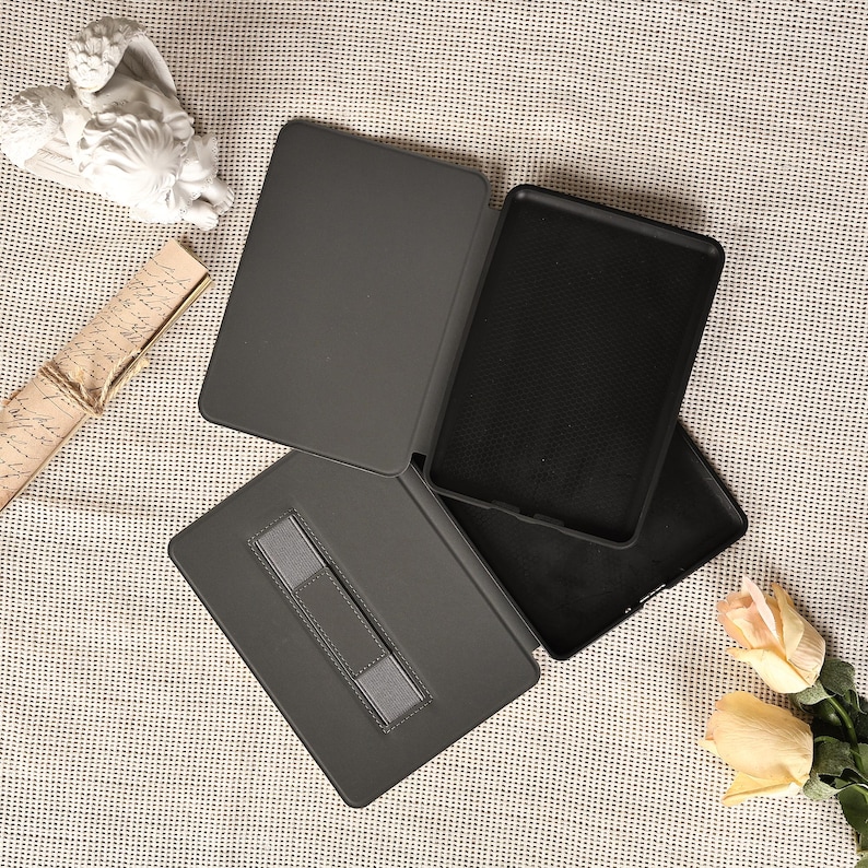 May include: A dark gray tablet case with a built-in hand strap. The case is open, revealing the interior and a black textured surface. The case is designed to protect the tablet from scratches and damage.