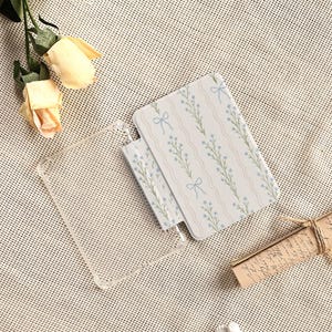 May include: A clear phone case and two notebooks with a floral pattern of blue flowers and bows on a white background. The notebooks have a wavy striped design. The image also includes two yellow roses and a scroll.