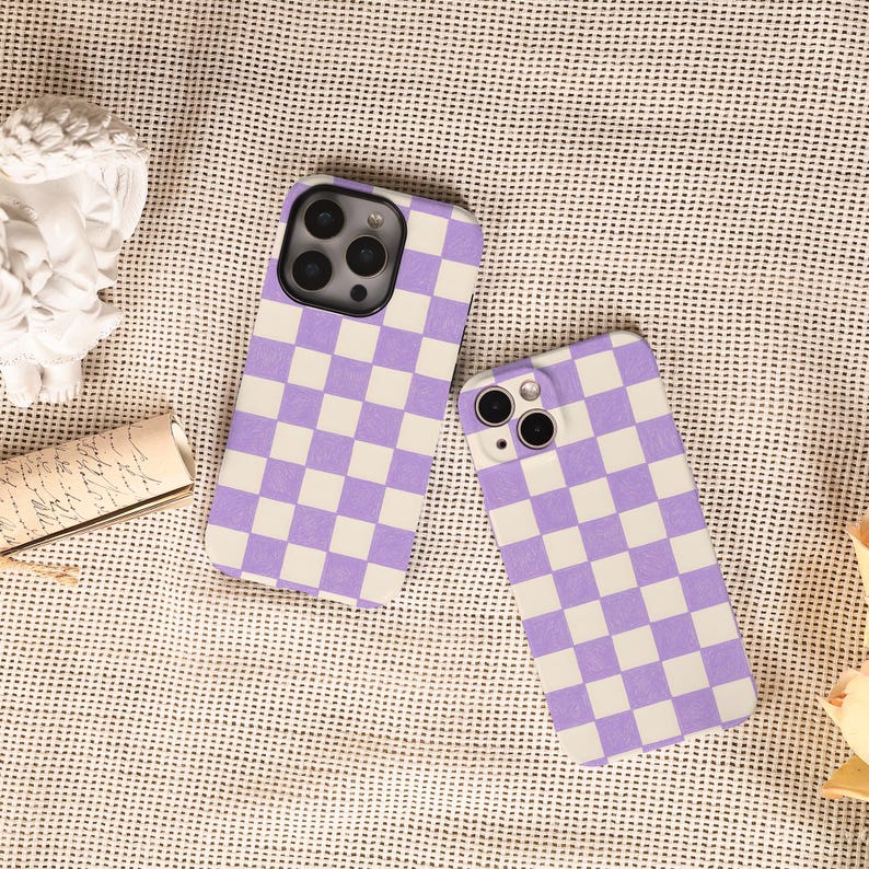 May include: Two phone cases featuring a purple and white chequered pattern. The cases are designed for a smartphone, with camera and button cutouts. The cases are displayed on a textured surface.