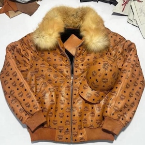 May include: A brown leather jacket with a fur collar and a matching baseball cap. The jacket features a repeating logo pattern and a zip closure. The jacket has a ribbed hem and cuffs.