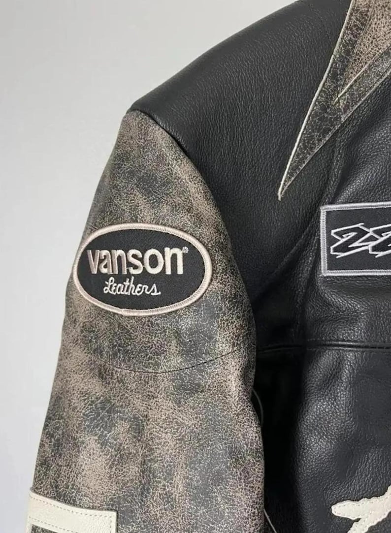 May include: Close-up of a black leather jacket with a distressed, textured sleeve. The jacket features a "vanson Leathers" patch and white accents. The jacket is a classic style, suitable for motorcycle enthusiasts.