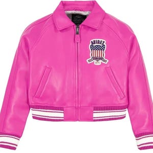 Puede incluir: Chaqueta bomber de cuero rosa brillante. Presenta un cuello cl&aacute;sico, cierre de cremallera y pu&ntilde;os y dobladillo a rayas blancas y rosas. Un parche bordado con el texto "AVIREX" y un dise&ntilde;o patri&oacute;tico adorna el pecho.