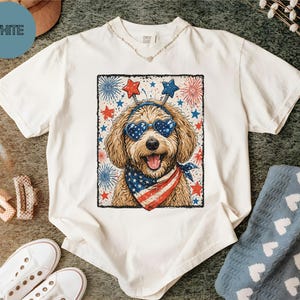 May include: White t-shirt featuring a dog wearing heart-shaped sunglasses, a bandana, and a headband with stars. The dog is surrounded by fireworks and stars. The word "WHITE" is in a blue circle in the upper left corner.