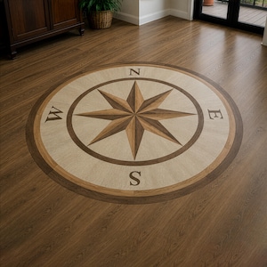 Peut inclure: Une rosace des vents circulaire incrustée dans un plancher en bois. La rosace présente une étoile centrale à huit branches dans des tons bruns et beiges, entourée d'une bordure. Les points cardinaux, N, E, S et W, sont marqués autour de l'étoile.