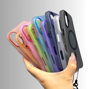 Könnte beinhalten: Eine Sammlung farbenfroher Handyhüllen in verschiedenen Farbtönen, darunter Rosa, Orange, Grün, Blau, Lila, Silber und Grau. Die Hüllen werden in einer Hand gehalten und zeigen ihre verschiedenen Farben und Designs. Jede Hülle hat ein schlankes, modernes Design.