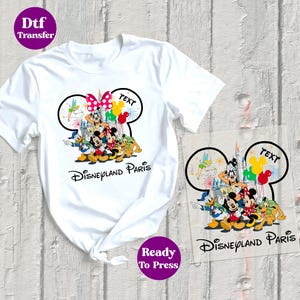 May include: White t-shirt with a vibrant graphic of Disney characters, including Mickey and Minnie Mouse, and the text "Disneyland Paris." The design incorporates a Minnie Mouse bow and balloons. A ready-to-press transfer is also visible.