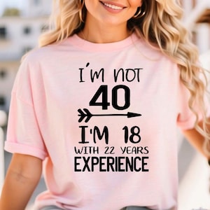 以下が含まれることがあります： 「I'm not 40, I'm 18 with 22 years experience」の黒い文字がプリントされた、薄いピンク色のTシャツ。 半袖でゆったりとしたフィット感があります。