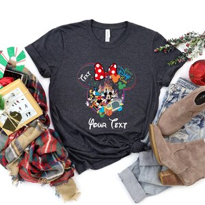 May include: Dark gray t-shirt featuring a colorful graphic of Disney characters, including Mickey and Minnie Mouse, with the text "Best Day Ever" and "Your Text". The design includes a red polka dot bow.