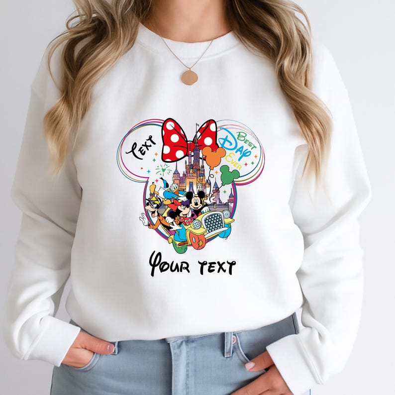 May include: White sweatshirt with a colorful graphic featuring Disney characters, a castle, and a red polka-dot bow. The graphic includes the text "Text" and "Best Day Ever" in a Mickey Mouse ear design, with space for custom text.