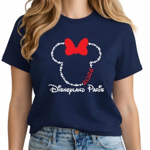 May include: Navy blue t-shirt featuring a white outline of a mouse head made of small hearts, with a red bow. The text "2026" is inside the head, and "Disneyland Paris" is written below in white.