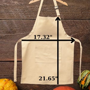 May include: A beige youth apron, 17.32 inches wide and 21.65 inches long, hangs on a wooden hanger. The word "Youth" is written in red at the top. The background is a wooden surface with gourds.