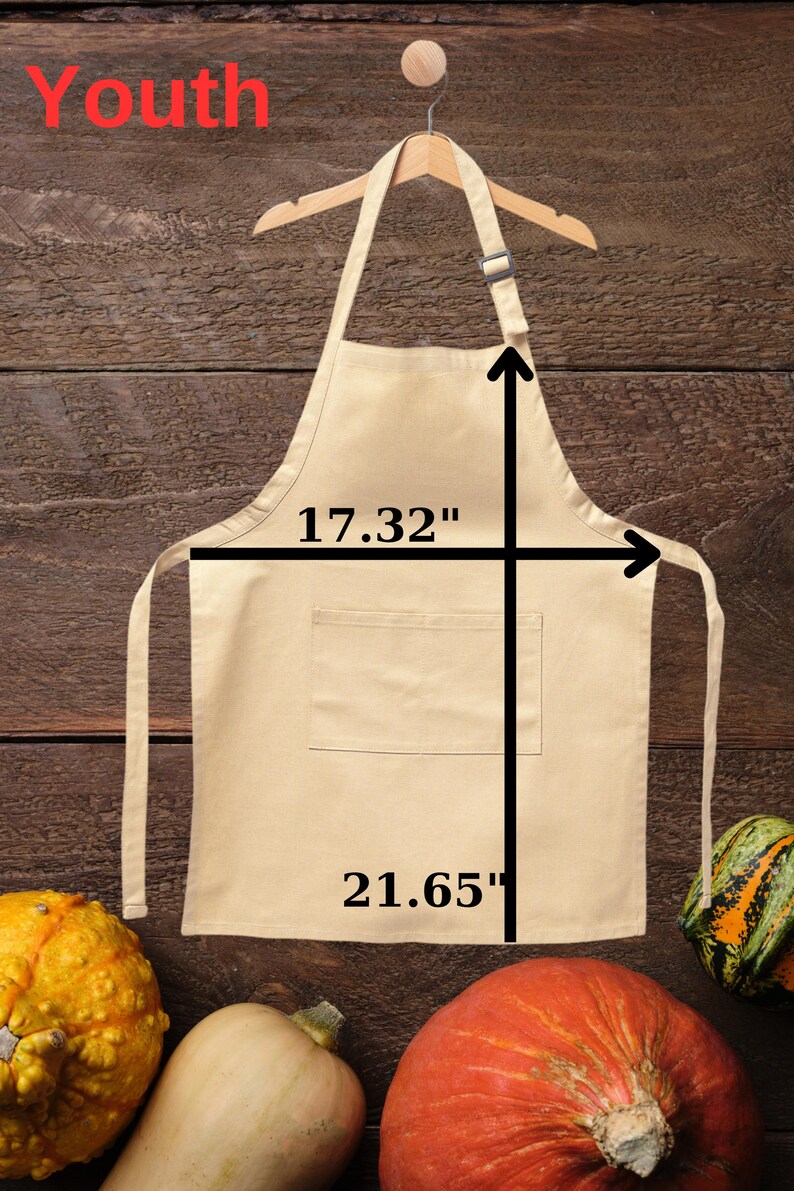 May include: A beige youth apron, 17.32 inches wide and 21.65 inches long, hangs on a wooden hanger. The word "Youth" is written in red at the top. The background is a wooden surface with gourds.