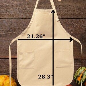 May include: A beige apron with two pockets, hanging on a wooden hanger. The apron measures 21.26 inches wide and 28.3 inches long. The word "Adult" is in red at the top. Gourds are at the bottom.