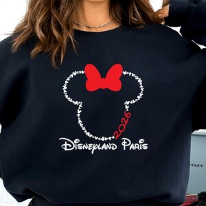 May include: Black sweatshirt featuring a white outline of a mouse head with a red bow. The year "2026" is in red, and the words "Disneyland Paris" are in white. The sweatshirt is a casual style.