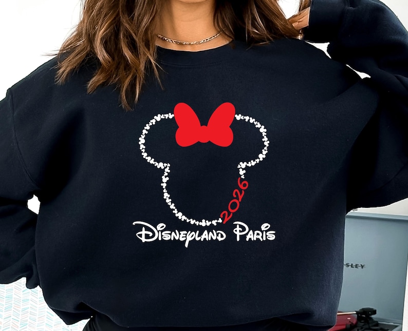 May include: Black sweatshirt featuring a white outline of a mouse head with a red bow. The year "2026" is in red, and the words "Disneyland Paris" are in white. The sweatshirt is a casual style.